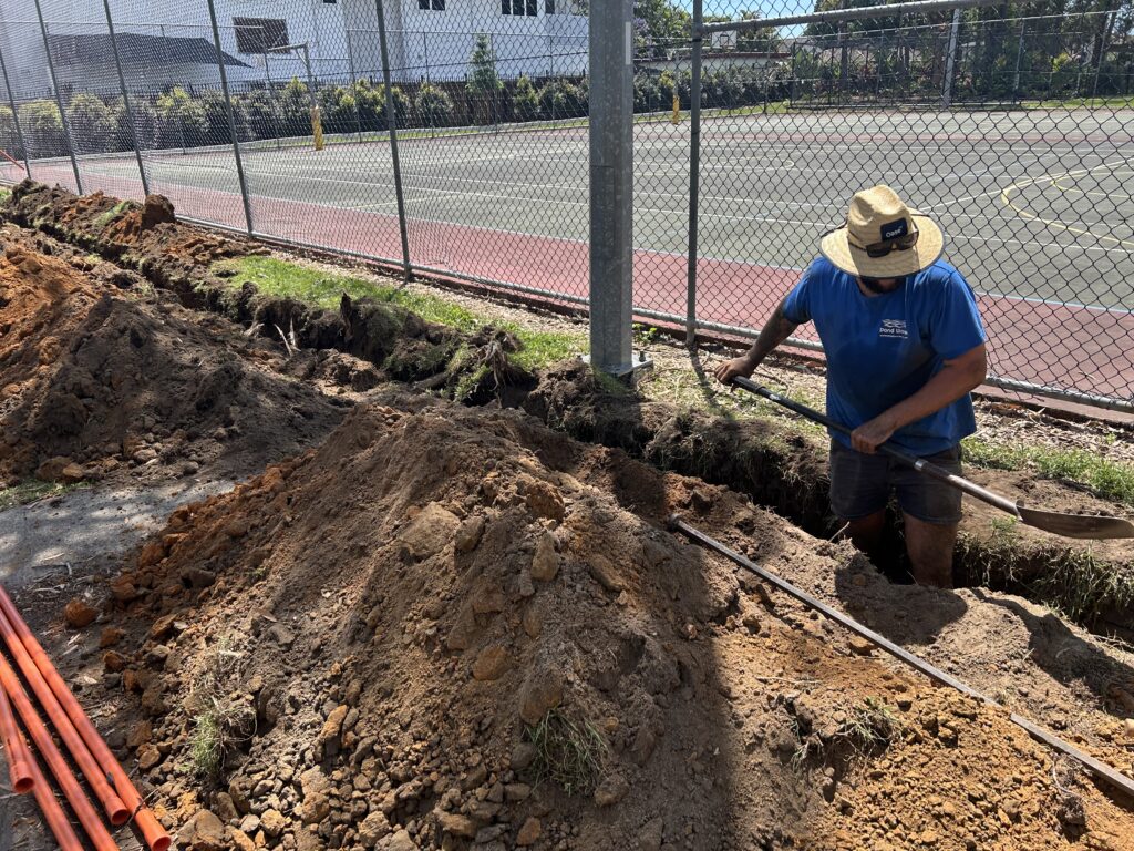 Sean digging trench for water supply installation at Kallangur State School pond construction site