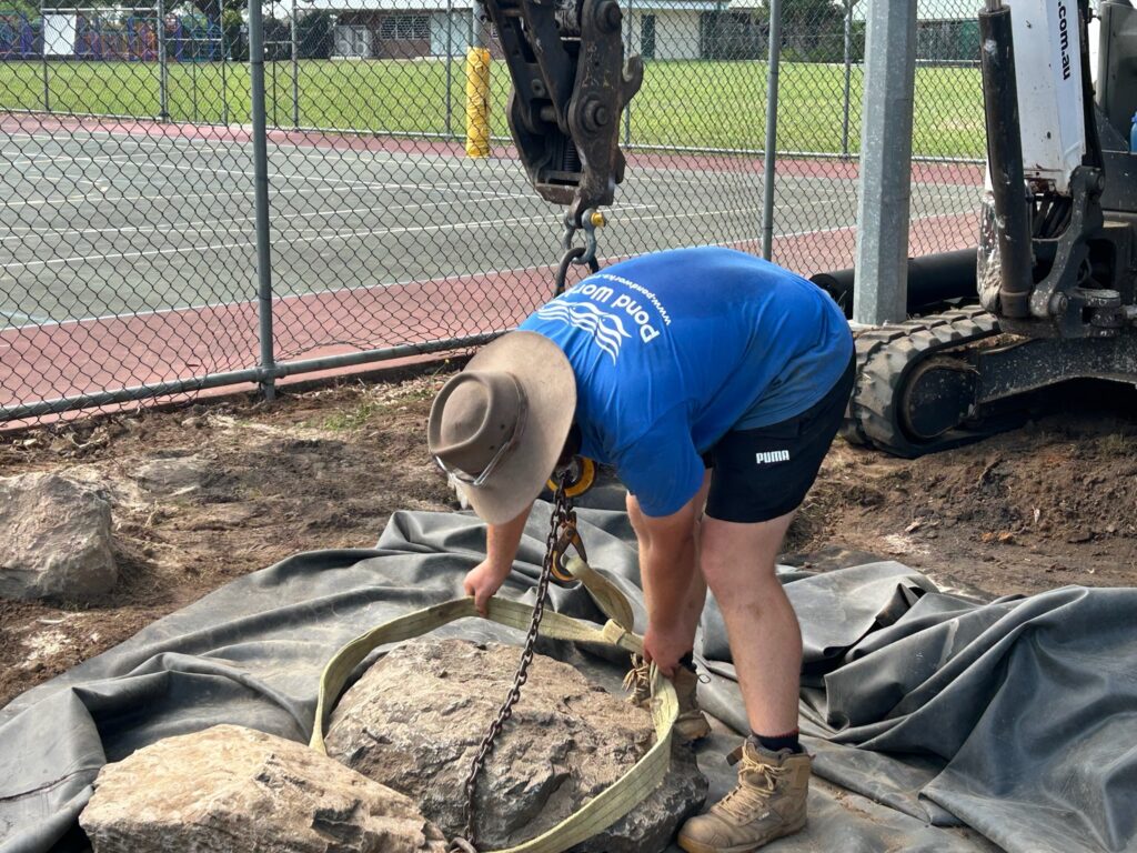 Pond Works team member preparing to sling large rock during pond construction at Kallangur State School
