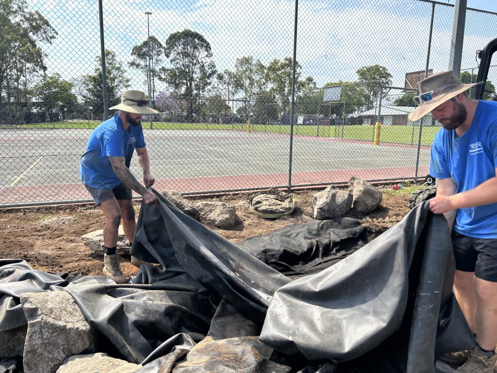 Sean and Bailey positioning pond liner in place during construction at Kallangur State School pond and stream project