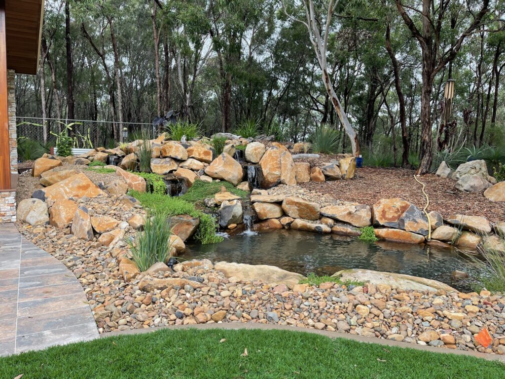 Natural bushside billabong pond with twin waterfalls and basalt boulder water feature in Burbank, Queensland, Australia.