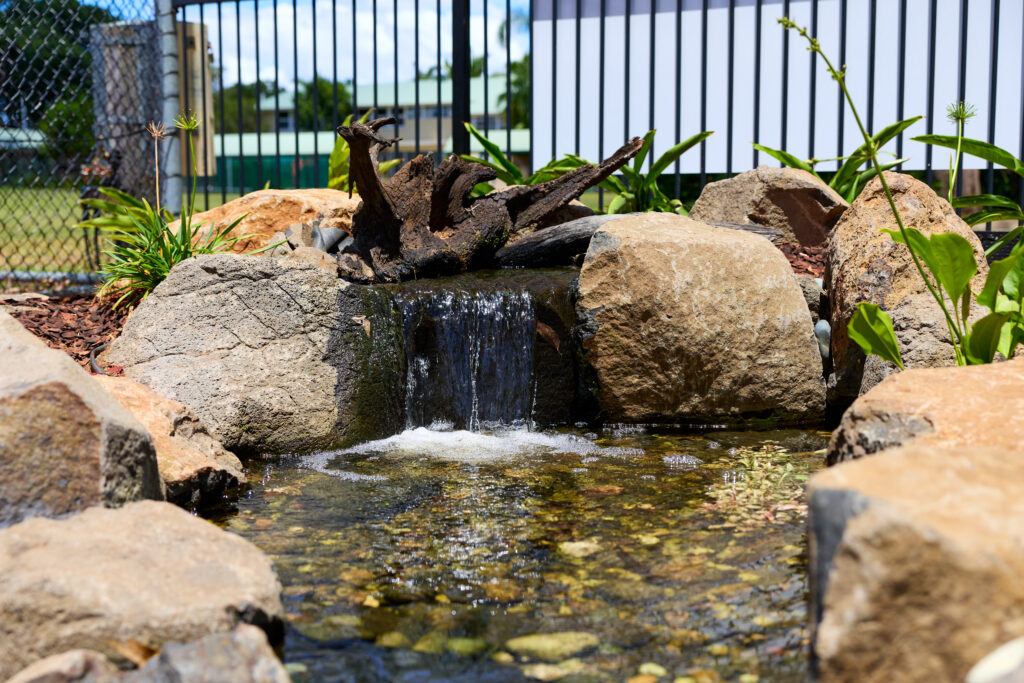 Water trickling over rocks into a small garden pond surrounded by stones and greenery.