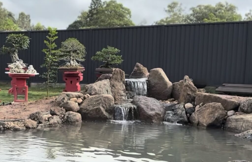 A Japanese-inspired garden waterfall built by Pond Works, featuring natural stone cascades flowing into a crystal-clear pond surrounded by carefully placed boulders and lush planting, creating a peaceful and authentic landscape.